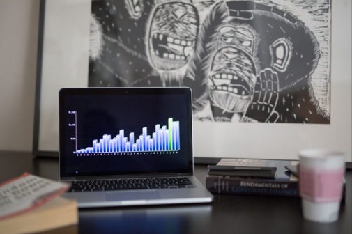 Dator med en graf på skärmen bredvid en bok och en kaffekopp på ett bord. Foto: Creative commons